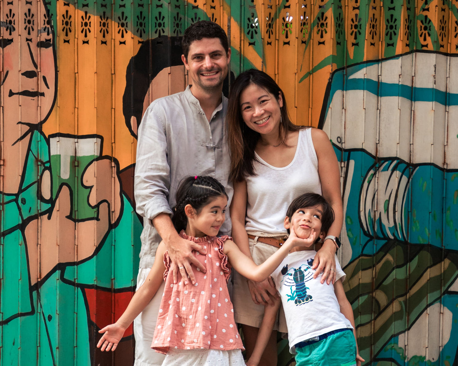a family of four with a cheeky sister pinching her brothers cheeks. Taken in front of a Hong Kong metal shutter door.