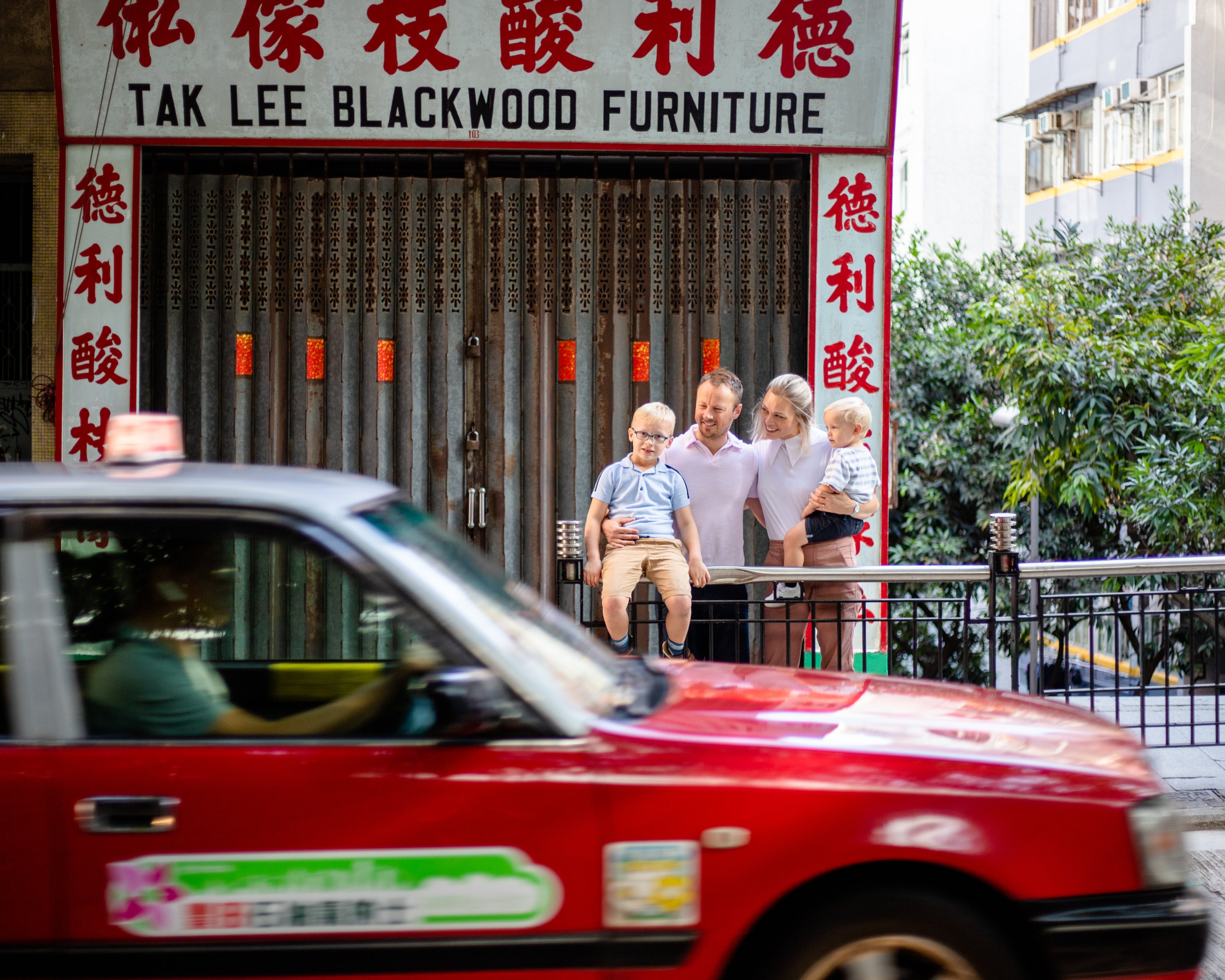 Family photo Hong Kong with a red Hong Kong taxi driving past 