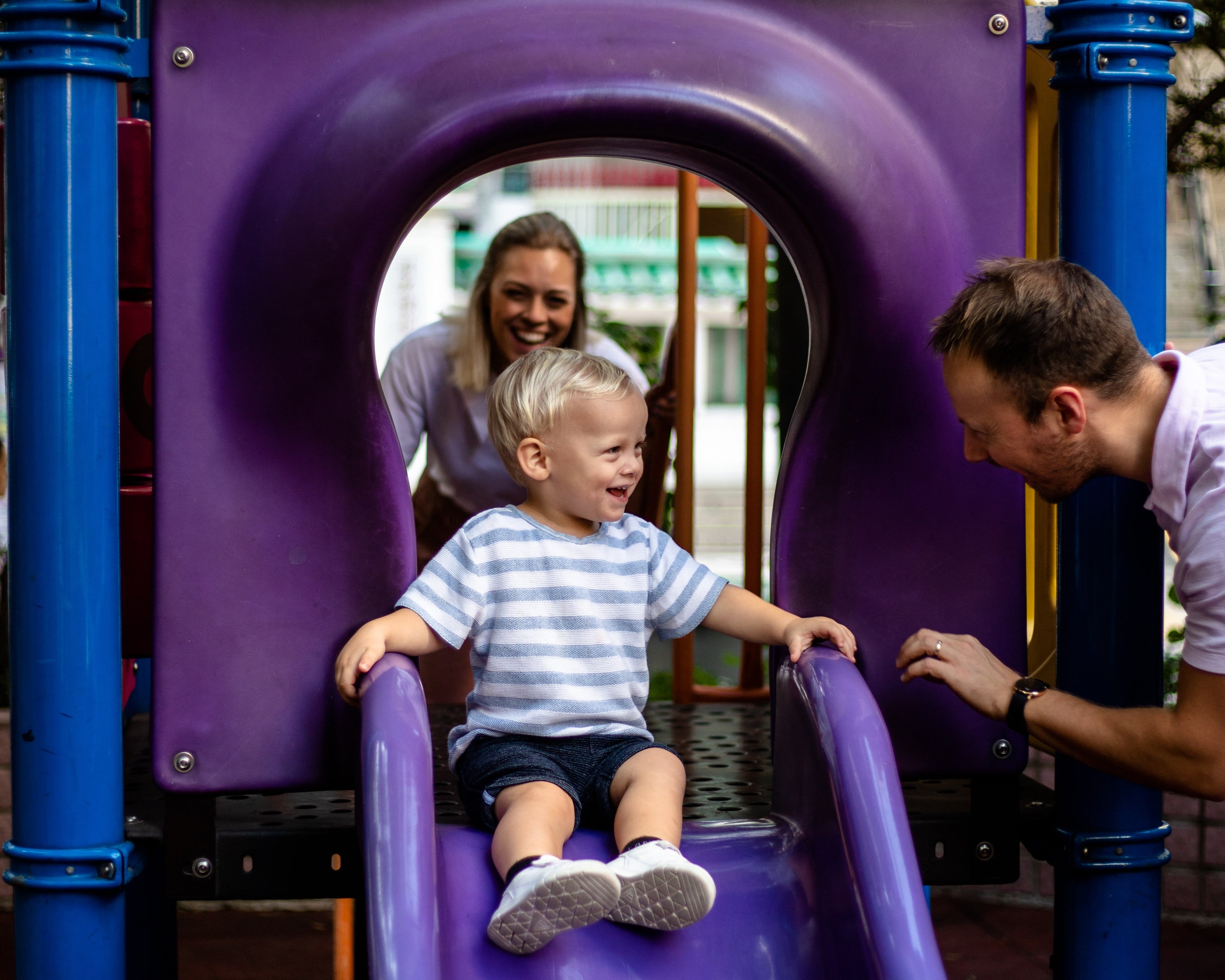 Mom and dad playing on a purple slide with their son in a hong kong park 