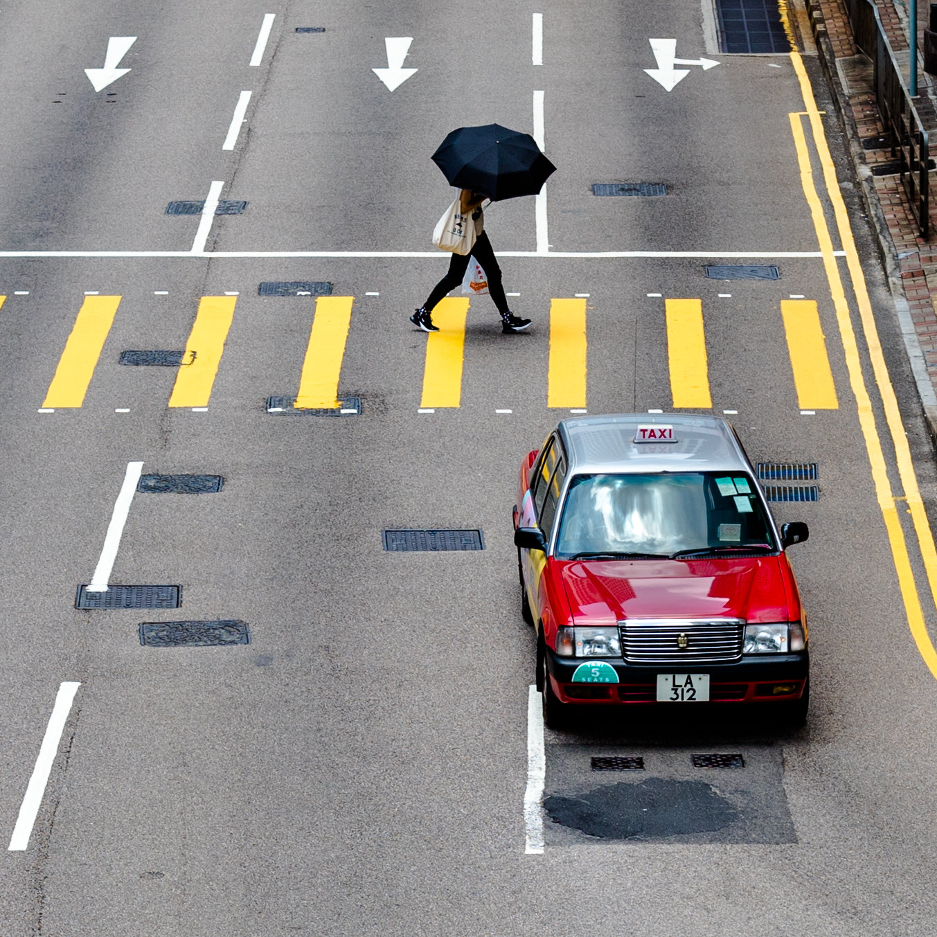 exploring central and taking a photo from above of a red taxi going by and a person with an umbrella in the cross walk