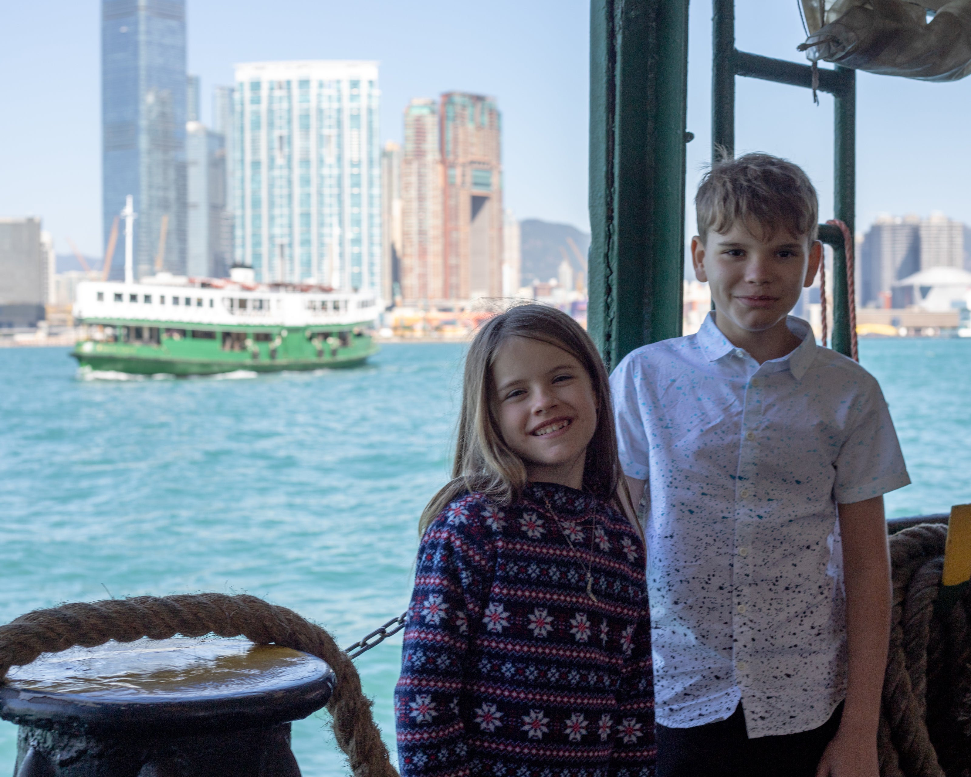 a sister with her big brother riding the hong kong star ferry with another star ferry in the background